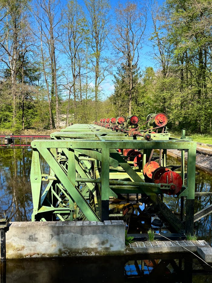 Green industrial machinery with red details over water in a forested outdoor setting.